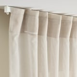 Light beige sheer curtain with visible folds and a white curtain rod. Allows light and shapes to filter through, ideal for wider windows.