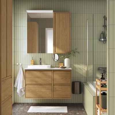 Modern bathroom with green walls, wooden vanity, white sink, and tall mirror.