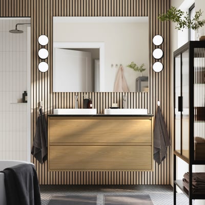 Modern bathroom with light wood ÄNGSJÖN vanity, two sinks, large mirror, black accents, and hanging towels. Clean, minimal design.