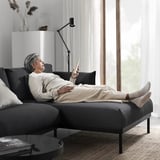 Person using smartphone on modern ÄPPLARYD sofa near window.