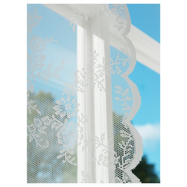 White lace-like floral net curtains with scalloped edges, suspending from a rod, allowing light to philtre through and offering partial privacy.