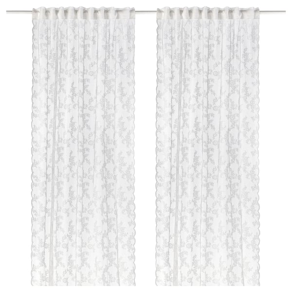Two white lace curtains hang side by side, featuring a delicate floral pattern and scalloped edges.