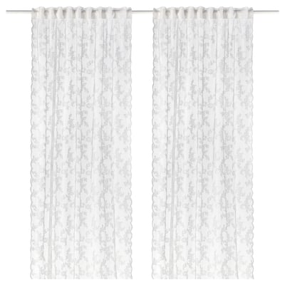 Two white lace curtains hang side by side, featuring a delicate floral pattern and scalloped edges.