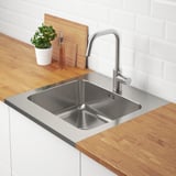 Stainless steel kitchen sink with a faucet, set in wooden countertop. Plant and oil bottle sit on the counter.