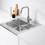 Stainless steel sink with a faucet, set in a white countertop against a tiled wall. Includes a pre-drilled hole for the mixer tap.