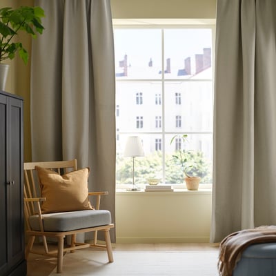 Bright room with large ANNAKAJSA light grey curtains, a wooden chair, and a windowsill decorated with a lamp and plant.