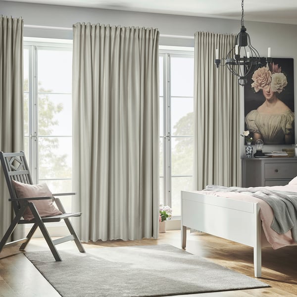 Minimalist bedroom with high, light grey ANNAKAJSA room-darkening curtains, a wooden chair, white bed, and large art print.