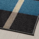 A modern striped rug with blue, grey, and beige colors laid on a wooden floor.