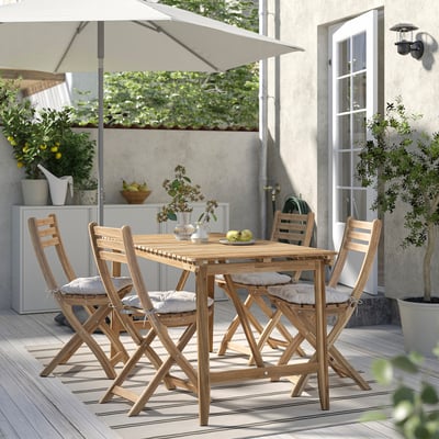 Outdoor patio set: rectangular acacia table, four matching chairs with white cushions, striped rug under, plants, wall hanging lamp.