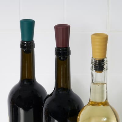 Three wine bottles with colored stoppers: green, red, and yellow, preventing leakage and preserving taste.