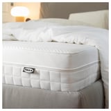 Close-up of a white IKEA mattress on a bed, showcasing its textured surface and handles.