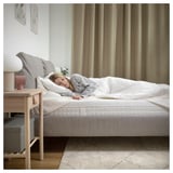 A person sleeping peacefully on an ÅVABERG white mattress with grey bedding in a cozy bedroom.