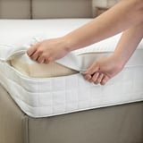 Person zipping up a white mattress cover, highlighting the removable feature for easy cleaning.