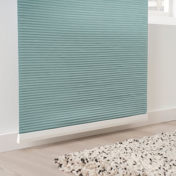 Teal sheer curtain on white wall allows diffused light, over textured rug on light wood floor.