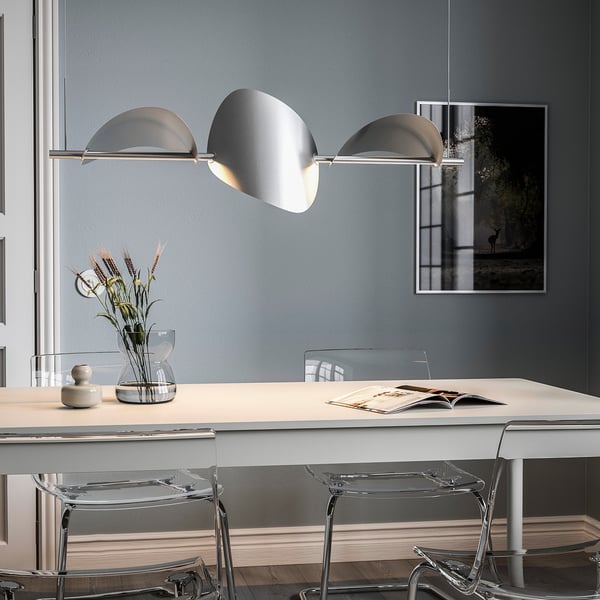 Modern BACKSTÖRN lamp over dining table, illuminating books and flowers.
