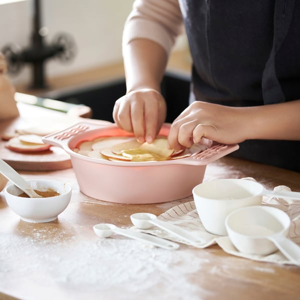 Person placing apple slices in pink silicone cake pan on table with bowls.