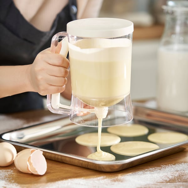 Person pours batter from a clear jug into a muffin tin, demonstrating the precise dispensing feature of the BAKTIDER measuring and dispensing jug.