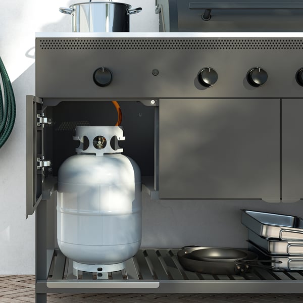 Gas grill cabinet with propane tank, knobs, and skillet.