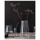 Clear glass vase with dried flowers on wooden table. Minimalist decor with small glasses and bowl.