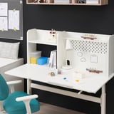 White kids adjustable desk with storage, pegboard, and lamp. Blue chair and colorful storage bins are visible.