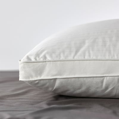 A well-made pillow with smooth, double-stitched edges sits on a grey sheet, showcasing its high-quality, soft fabric and plush filling.
