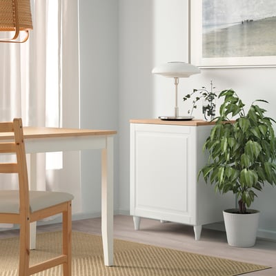 White BESTÅ unit beside dining table with plant & lamp, under large window.
