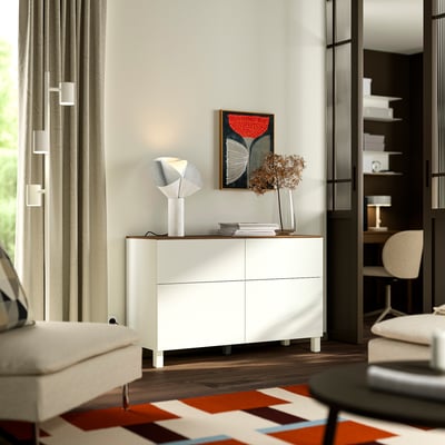 Modern living room with white BESTÅ sideboard, geometric lamp, abstract art, white curtains, and patterned rug.