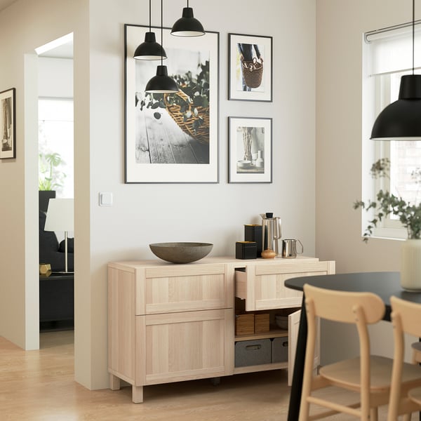 Light-filled dining area with light wood sideboard, black pendant lamps, framed wall art, open drawer, and chair.