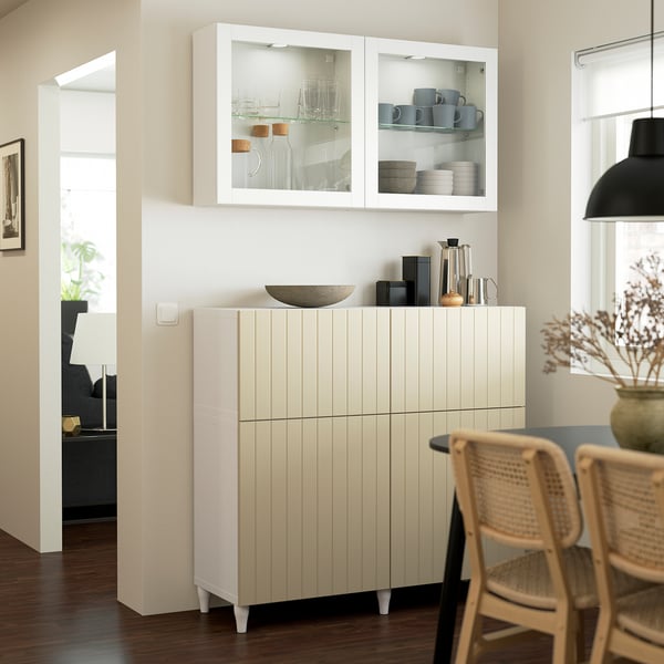 Modern kitchen with BESTÅ cabinet showing mugs, wooden countertop, and wicker chairs near a window.