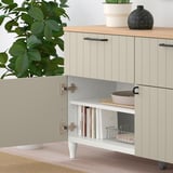 BESTÅ sideboard with open door, shelves, books, and bowls. Top with plants and vase, gray walls.