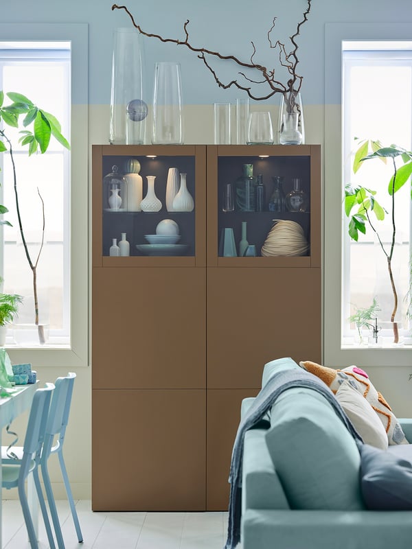 Modern room with blue walls, large windows, dark storage unit, vases, green plant, gray sofa.