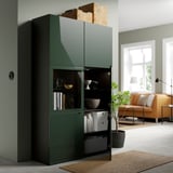 Dark green storage unit with glass doors displaying items, next to living area with couch and window.