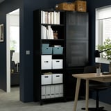 Black BESTÅ storage with shelves & glass doors, holding books, boxes, decor, in modern room with dark blue walls, next to desk & chair.