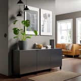 Modern living room with BESTÅ sideboard, plant, art, books, lamps, window, orange sofa.