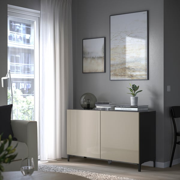 Modern living room with BESTÅ unit, art, plant, books, bowl, black chair, armchair by window.