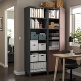 Black BESTÅ storage unit with shelves and grey boxes, near a wooden desk and chair in an office space.