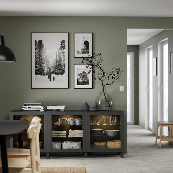 Modern living room with green walls, black sideboard, nature photos, and light wood chairs.