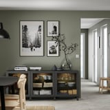 Modern living room with green walls, black sideboard, nature photos, and light wood chairs.