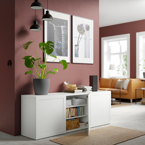 Modern living room with a white BESTÅ sideboard. It adjustable shelves, a soft-close door, and a large plant on top. Two framed photos hang above it.