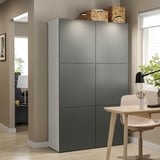 Modern grey BESTÅ storage unit in living room with wooden chair, lamp, and plant on desk.