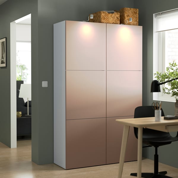 Large BESTÅ storage unit with pinkish-brown doors, black chair, and desk in minimalist room.