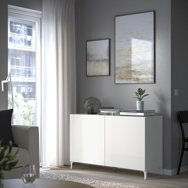 Modern living room with BESTÅ white cabinet, plant, books. Trendy, under abstract art and large window.