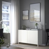 Modern living room with BESTÅ white cabinet, plant, books. Trendy, under abstract art and large window.