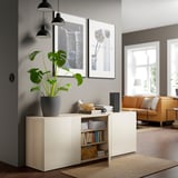 Modern living room with plant, books, speaker, and yellow sofa near window.