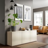 Modern living room with BESTÅ sideboard, plant, books, speaker, orange sofa, and large windows.
