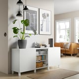 Modern sideboard with adjustable shelves, holding plants and books, beneath framed art, in a cozy living room.
