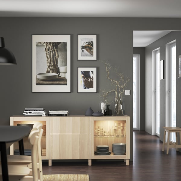 Modern dining area with wooden sideboard, glass doors, artwork, and dark chairs/tables.