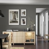 Modern dining area with wooden sideboard, glass doors, artwork, and dark chairs/tables.