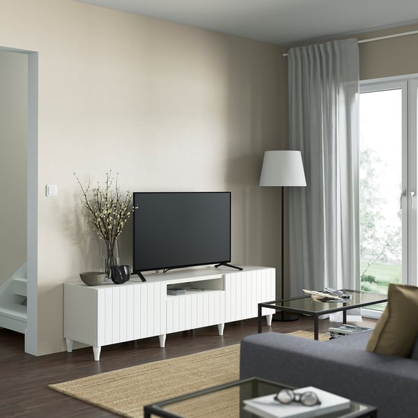 Modern living room with BESTÅ white tv bench, flat screen, flowers, grey curtains, and coffee table with magazines.