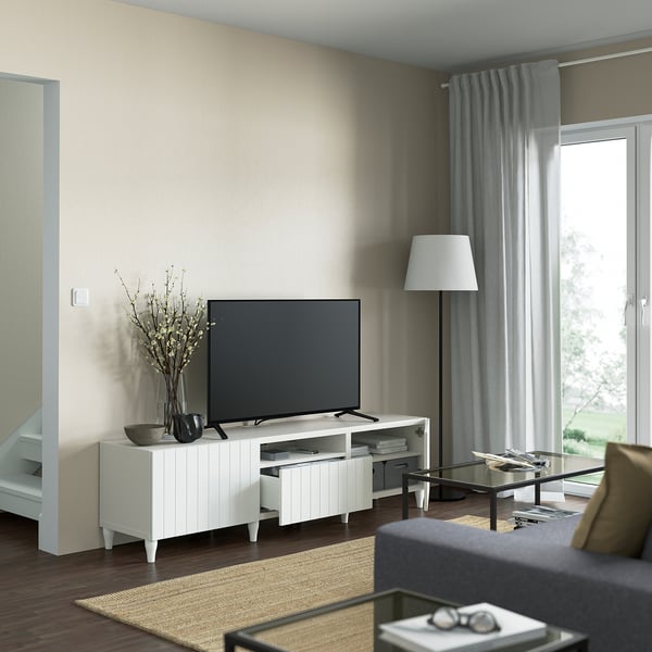 Modern living room with white BESTÅ tv bench. Flat-screen tv sits atop, with cable management visible at the back. Drawers below for storage.